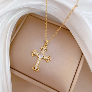 Macro shot of a gold cross necklace with clear zircons on beige jewelry box and white silk