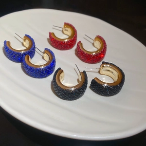 Macro detail of C-shaped geometric earrings with sparkling crystals in blue, red, and black