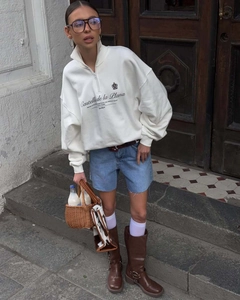 Street style shot of white half-zip sweatshirt with blue denim shorts and brown boots
