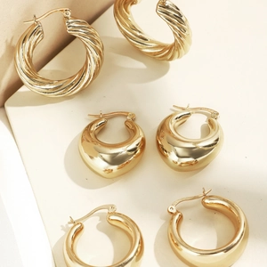 Dreiteiliges Set goldener geometrischer Ohrringe auf minimalistischem cremefarbenem Sockel