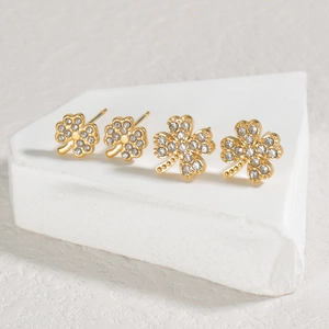 Detail of gold clover stud earrings with sparkling crystals on white stone display