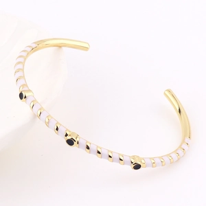 Detail of gold-plated open bangle with white enamel spiral texture and black polka dots