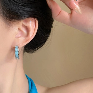 Détail d'une femme portant des boucles d'oreilles C bleu clair texturées et argent