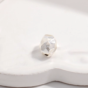 Macro shot of an irregular faceted S925 sterling silver bead on a white ceramic tray
