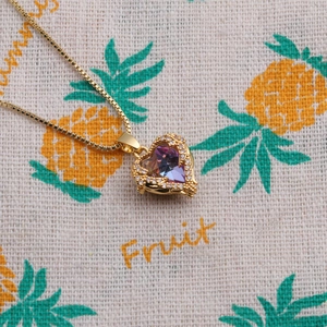 Collier cœur doré avec pierre violette et cristaux sur tissu décoratif