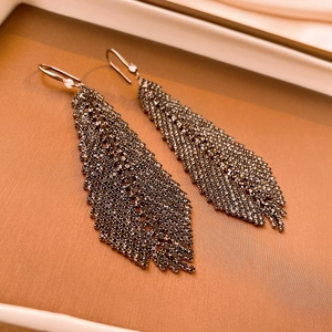 Detail of diamond-studded black feather leaf fringe earrings in a white jewelry box