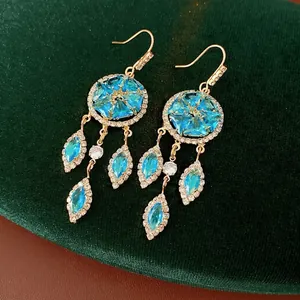 Vintage gold tassel earrings with blue zircon inlays on dark green velvet background
