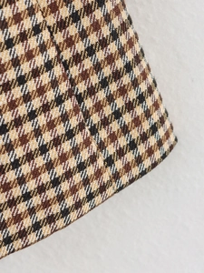 Makroaufnahme der klassischen braunen Hahnentritt-Stofftextur und Nähte am Damen-Blazer