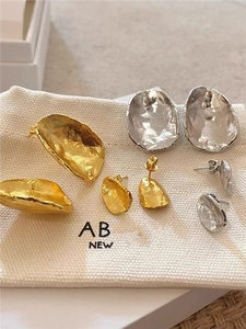 Macro view of textured irregular gold and silver organic shape metal stud earrings on canvas