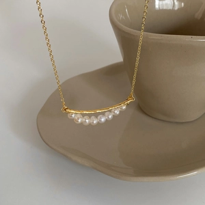 Minimalist gold necklace with a spiral bar and seven baroque freshwater pearls on ceramic