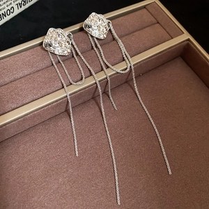 Macro detail of silver rose stud earrings featuring long multi-layer chain tassels on velvet