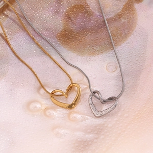 Macro shot of gold and silver heart pendants with thin chains on a water droplet surface