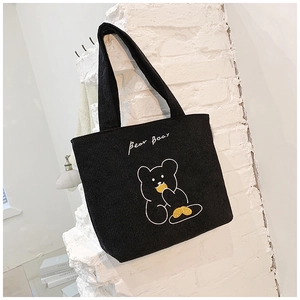 Detail of black corduroy tote bag featuring a cute embroidered bear and text on white wall