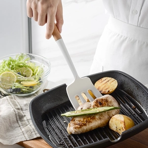 Cream silicone spatula with wooden handle flipping roasted chicken in a black pan