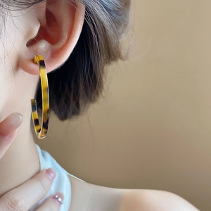 Close-up of tortoise shell resin C-shaped hoop earrings worn with gold metal edges