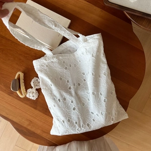 Detailed view of floral eyelet embroidery on white cotton tote bag texture