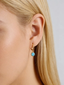 Detail of gold hoop earrings with round blue turquoise pendant on a female model
