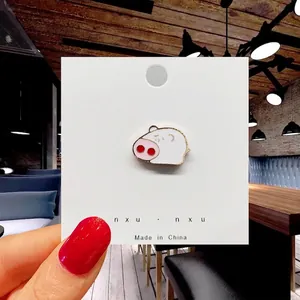 Detailed view of a cute pink and white enamel pig brooch badge on a paper display card