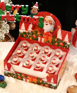 Coffret cadeau de 12 mini boules à neige Père Noël disposées sur un décor de neige blanche