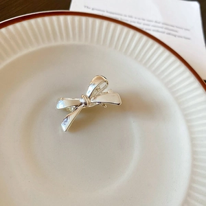 Polished silver metal bow hair clip displayed on a minimalist striped ceramic plate