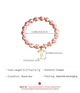 Dettaglio del bracciale con perline di ceramica a fiori rosa e ciondolo a fiocco dorato