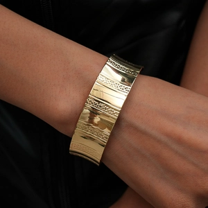 Détail d'un large bracelet manchette doré avec rayures texturées et finition polie