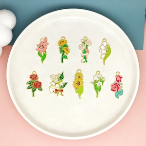 Detailansicht von neun bunten Emaille-Blumenanhängern mit Goldrand auf einem Tablett