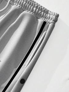 Detail of light grey joggers with side stripes and functional snap button closure
