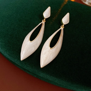 Detailed view of vintage gold-rimmed white enamel teardrop earrings on green velvet surface