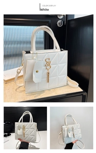 Detailed view of white quilted crossbody bag with gold logo, tassel, and mini pouch accessory