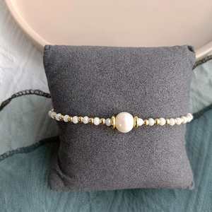 Elegant natural freshwater pearl bracelet with golden beads on a grey velvet cushion