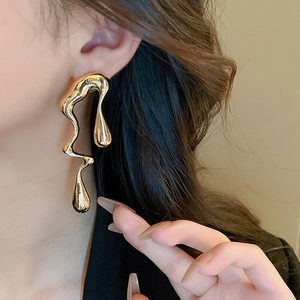 Close-up of long irregular liquid-style gold lava earrings worn by a model