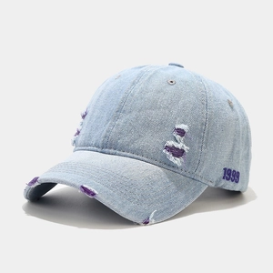 Détail d'une casquette en denim délavé avec broderie 1999 violette et bords usés