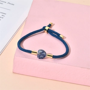 Detail of blue woven rope bracelet with heart-shaped natural stone and gold metal beads