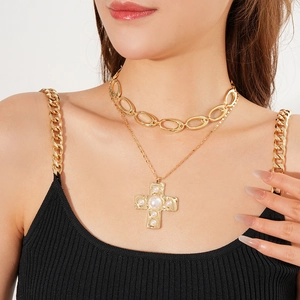 Close-up of layered gold chain necklaces with a pearl-inlaid cross pendant on a model