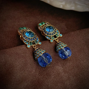 Vintage gold drop earrings with blue faceted crystal on a brown velvet background