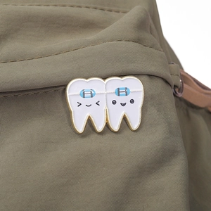 Detailed view of creative tooth-shaped enamel pins pinned on a green canvas bag