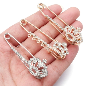 Detailed close-up of three crown-shaped crystal safety pins in gold, silver, and rose gold