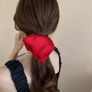 Elegant red silk satin scrunchie with large bow design on a female model with dark hair