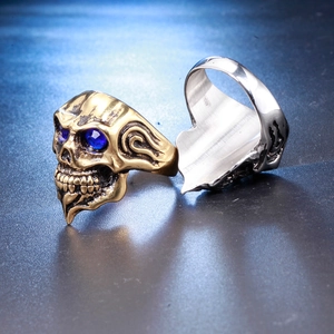 Detailed view of gothic skull rings in gold and silver finish with blue gemstone eyes