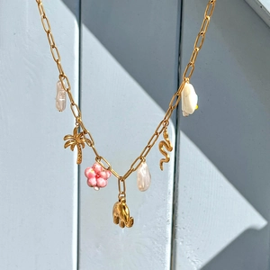 Macro detail of gold necklace featuring pearl, coconut tree, and snake charms on wood