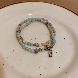 Macro detail of agate stone beads with a silver bell and 'Lucky' charm on a ceramic plate