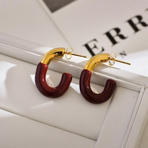 Close-up of gold and burgundy C-shaped stud earrings on a white leather texture display