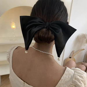 Detail of a large black satin bow hair clip with elegant hanging pearl charms for women