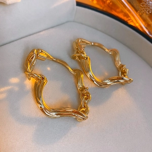 Irregular twisted golden earrings presented in a beige velvet jewelry box with warm lighting