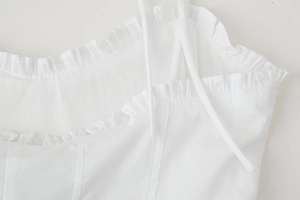 Detailed close-up of white dress with spaghetti straps and delicate ruffle trim on neckline