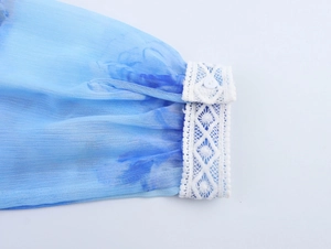 Dettaglio della manica in chiffon sfumato blu con bordo in pizzo bianco e bottone