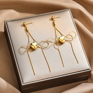 Detailed view of long gold drop earrings featuring elegant bow and heart pendants