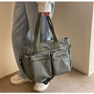 Detail of green corduroy crossbody bag showing ribbed texture and multiple zip pockets