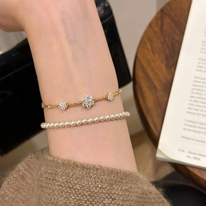 Detail of luxury gold rhinestone snowflake charm and elegant white pearl bracelet on wrist